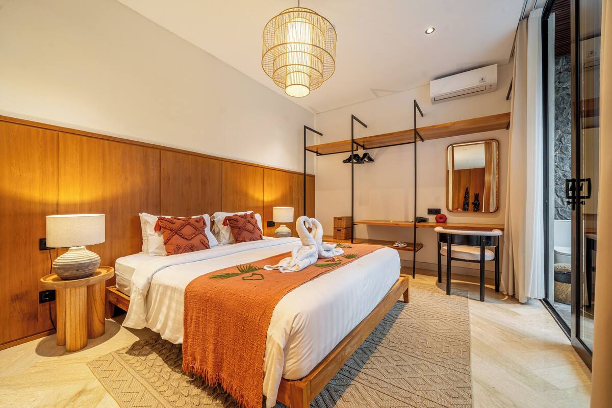 A modern hotel room with a large bed, a desk, a mirror, and a view of the outside.