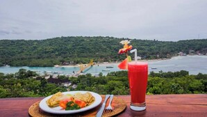 Una mesa con un plato de comida y una bebida, con vistas a un paisaje costero con vegetación y un puente.