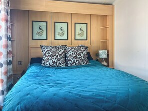Un dormitorio con colcha azul, dos almohadas estampadas, cabecera de madera y tres cuadros con imágenes de pavos reales enmarcados.