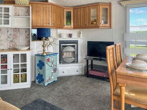 Un espacio habitable pequeño con armarios de madera, un televisor, una mesa de comedor y un aparador decorativo azul.
