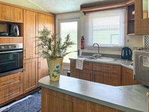 Una cocina con armarios de madera, un refrigerador Breville, un lavamanos y una ventana con persianas.