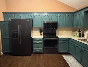 Eine Küche mit türkisfarbenen Schränken, einem schwarzen Kühlschrank, einer Mikrowelle und einem Backofen.