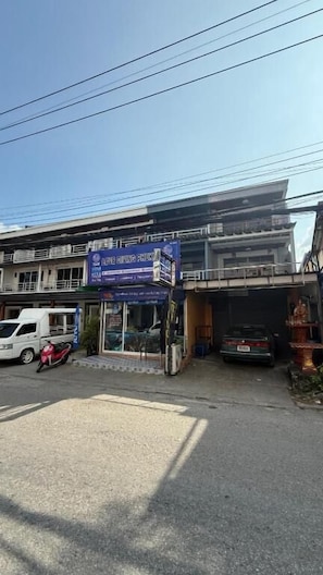 A building with a blue sign, a parked motorcycle, and a car. - Chalong Paradise Guesthouse (Rawai)