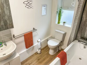 A bathroom with a toilet, sink, and bathtub, a towel rack, and a window with a plant. - 2 bedroom accommodation in Weymouth (Weymouth)
