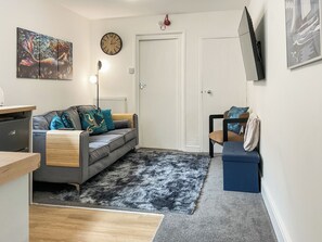 A living room with a grey sofa, a blue chair, a black and white rug, a clock, and a painting on the wall. - 2 bedroom accommodation in Weymouth (Weymouth)