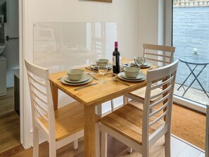 A dining table set with plates, bowls, wine glasses, and cutlery, surrounded by white chairs, with a window view. - 2 bedroom accommodation in Weymouth (Weymouth)