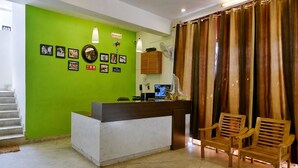 A reception desk with a green wall, framed pictures, a 'CHECK OUT' sign, a computer, and wooden chairs. - Hotel GSA and BANQUET (Haridwar)