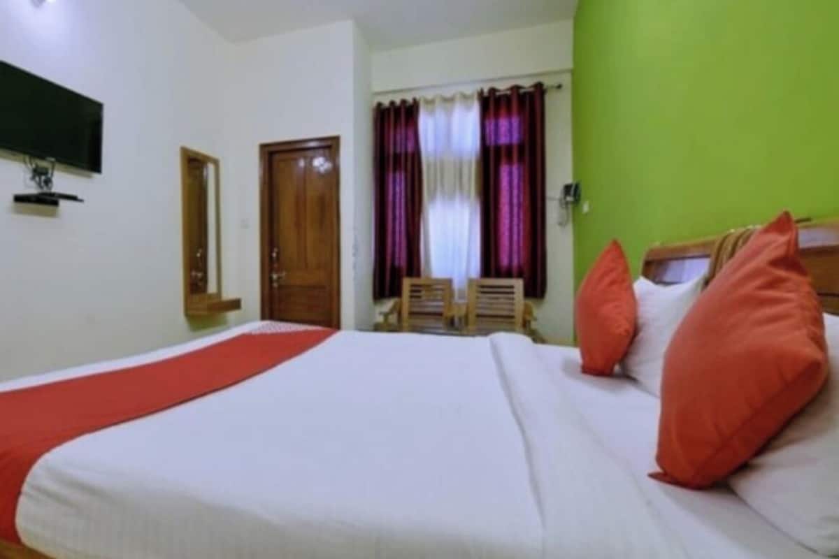 Ein Hotelzimmer mit einem Bett, einem an der Wand montierten Fernseher, einem Fenster mit Vorhängen und einer Tür.