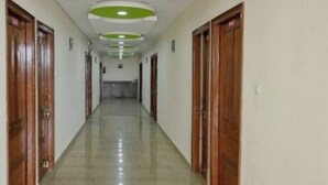 A long, narrow hallway with wooden doors on both sides and a tiled floor. - Hotel GSA and BANQUET (Haridwar)