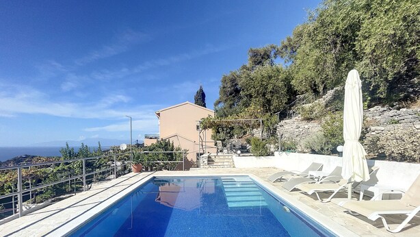 En swimmingpool med fri utsikt över havet, en stenmur och en byggnad med ett sluttande tak.