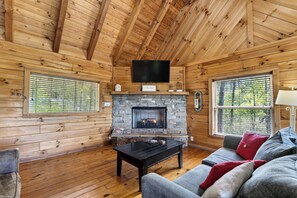 A log cabin interior with a stone fireplace, wooden walls, a flat-screen TV, and a sofa.