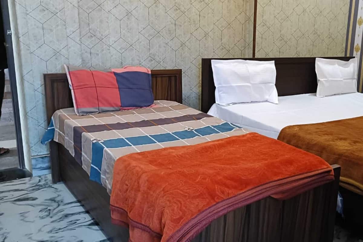 A double bed with a patterned bedspread and two pillows, a nightstand with a lamp, and a window with curtains.