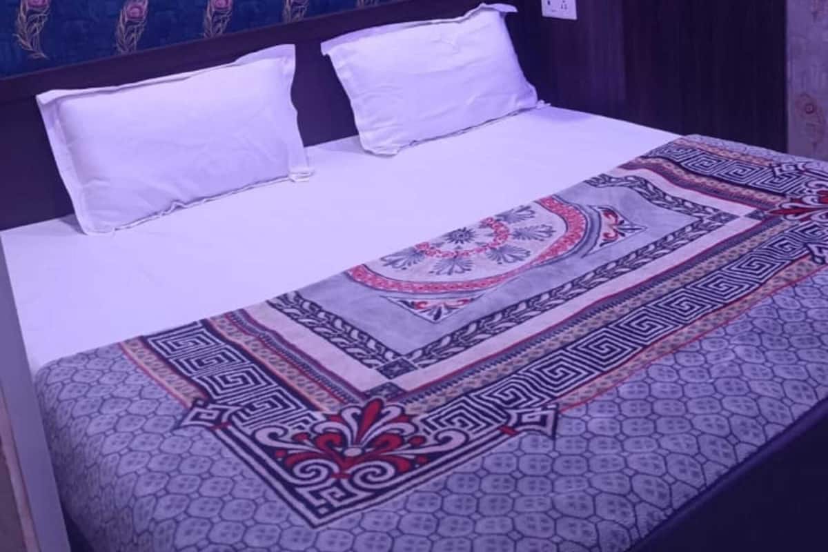 A bed with white bedding, a patterned bedspread, and a dark wardrobe in a room with patterned wallpaper.