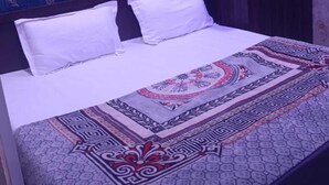 A bed with white bedding, a patterned bedspread, and a dark wardrobe in a room with patterned wallpaper.
