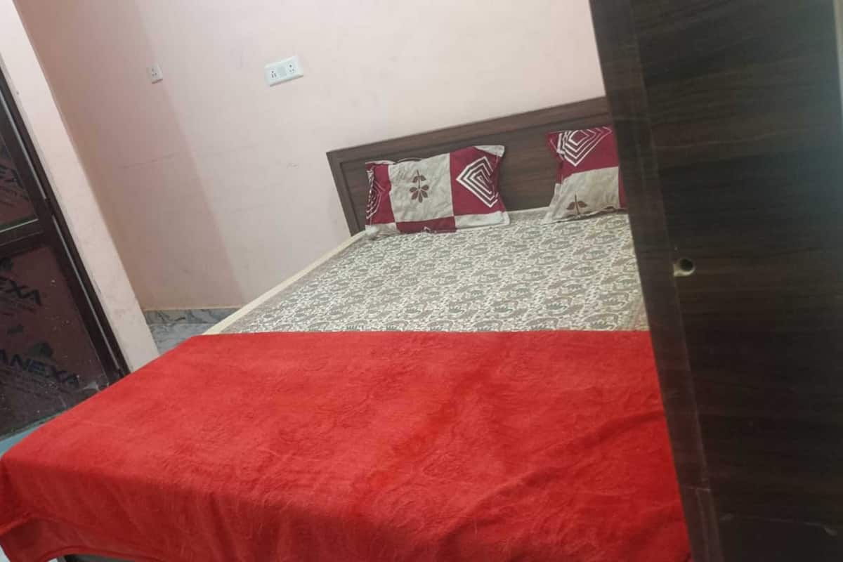 A room with a bed, a red bedspread, patterned pillows, a wooden headboard, and a door with a metal frame.