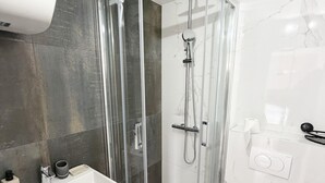 Un baño moderno con ducha de vidrio, un lavamanos blanco y azulejos de mármol.