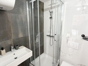 Ein modernes Badezimmer mit einer gläsernen Dusche, einem weißen Waschbecken und Marmorfliesen.