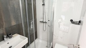 Un baño moderno con ducha de vidrio, lavamanos blanco y retrete.