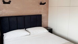 Una cama con sábanas blancas, cabecera oscura y una toalla blanca sobre la cama.