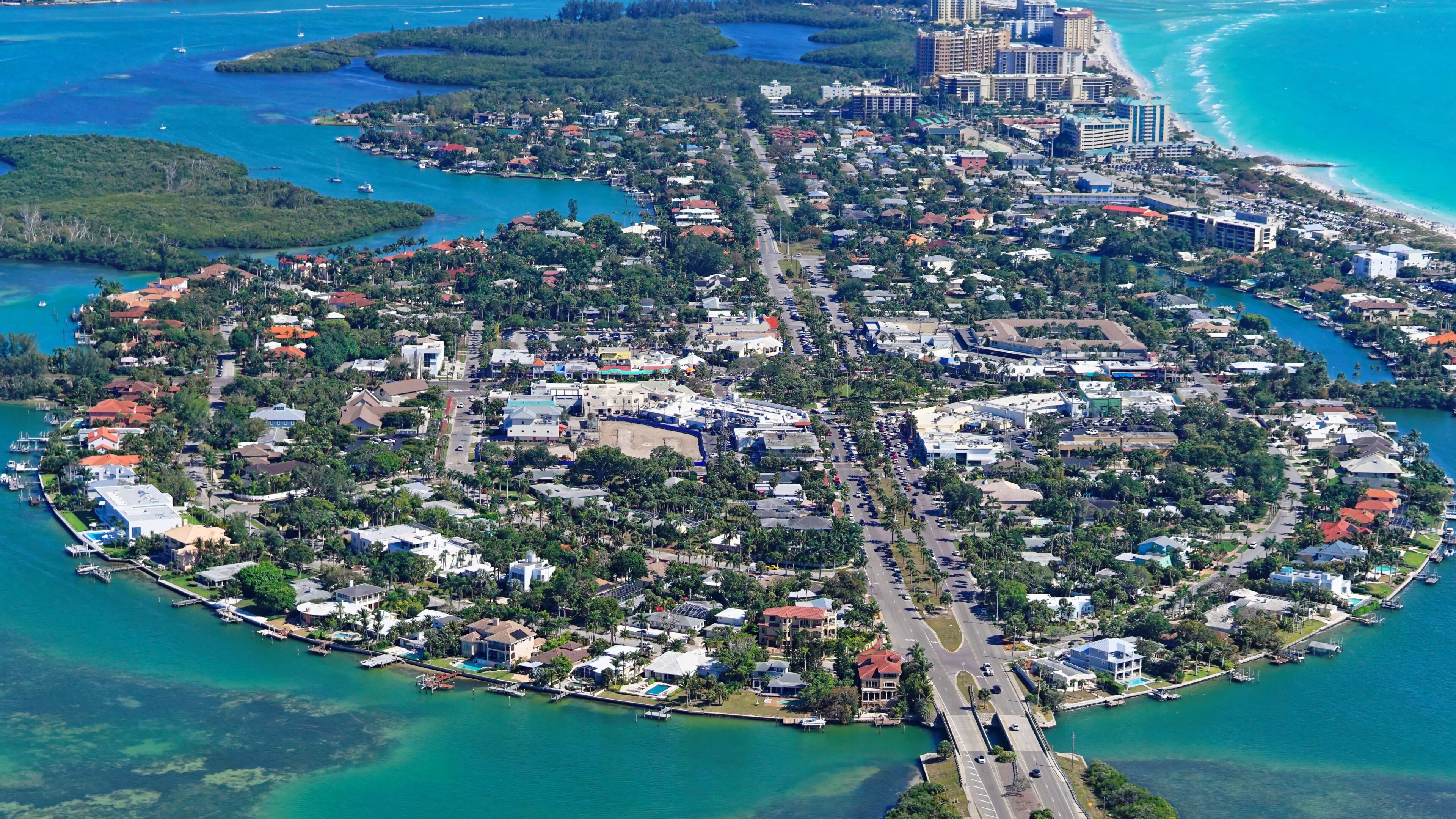 An aerial view of a coastal city with a central road, surrounding residential areas, and a marina.