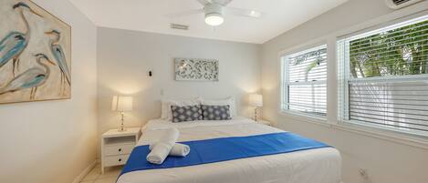 A bedroom with a bed, nightstands, a ceiling fan, a window with blinds, and a wall art piece.