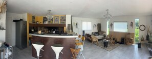 Eine moderne Küche mit Kochinsel, Barhocker, einer Essecke mit einer Couch und einem großen Fenster.