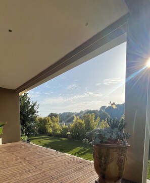 Eine Holzterrasse mit Blick auf einen Garten und eine entfernte Hügelkette.