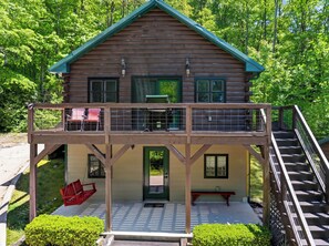 Eine zweistöckige Holzhütte mit einem Balkon, einer Veranda mit Schaukel und einer Treppe zum Obergeschoss.