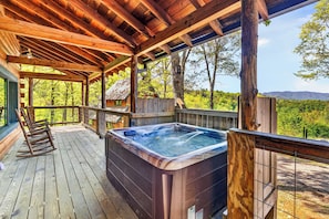 A wooden deck with a hot tub, rocking chairs, and a view of a forested area. - Sleeps 30 | 5 Cabins + Hot Tubs + Firepit + Views | Mtn Views + Smokies Access (Townsend)