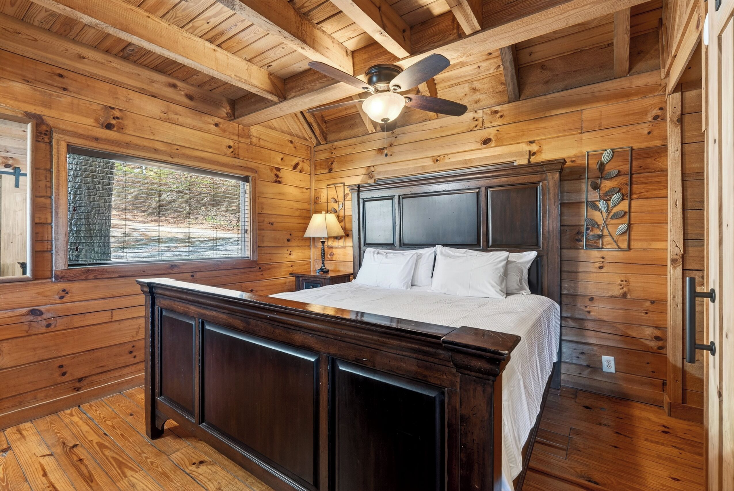 A wooden cabin bedroom with a bed, nightstand, lamp, and ceiling fan.