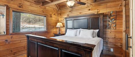 A wooden cabin bedroom with a bed, nightstand, lamp, and ceiling fan.