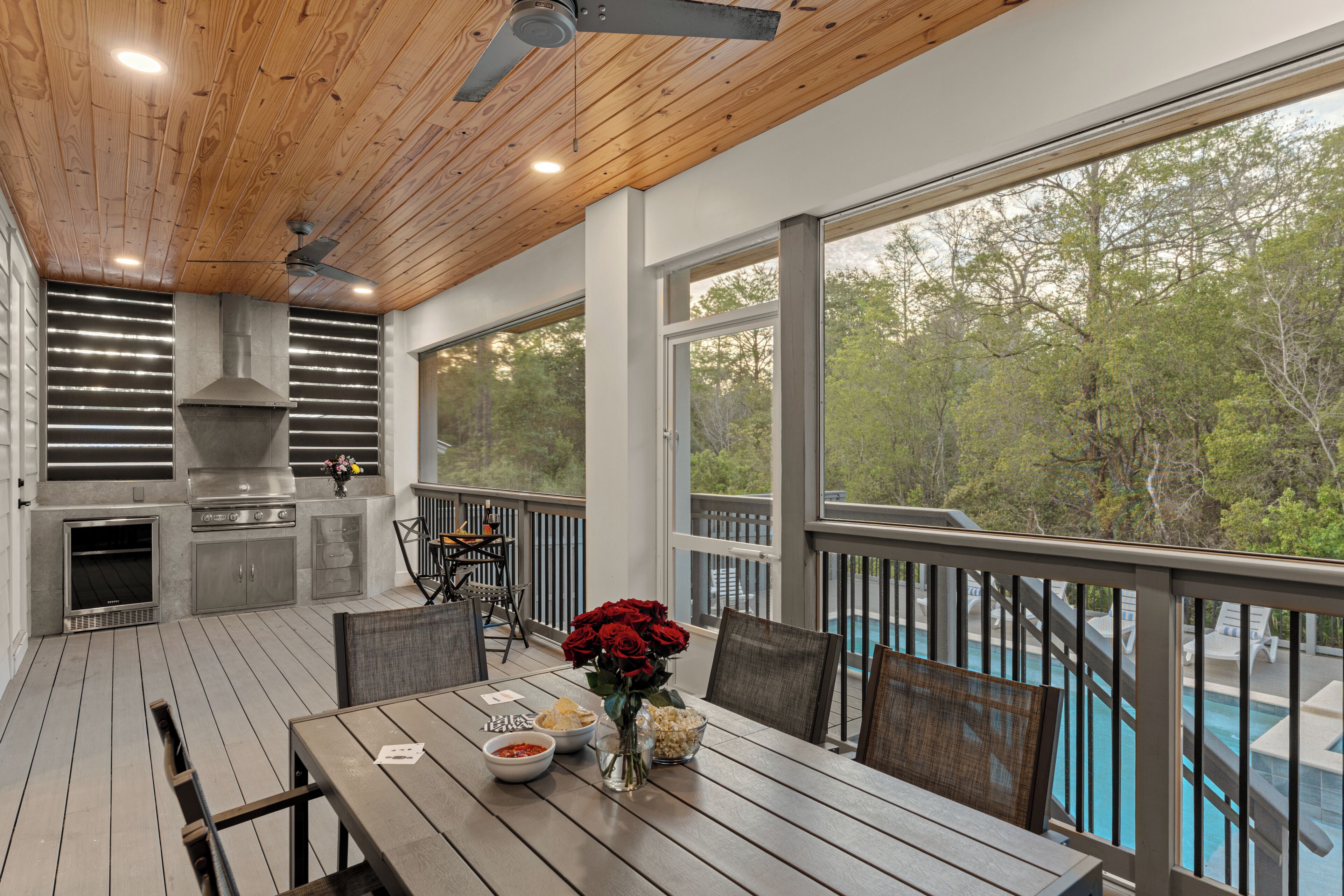 Une terrasse extérieure avec une table à manger, des chaises, un barbecue et une vue sur une piscine.
