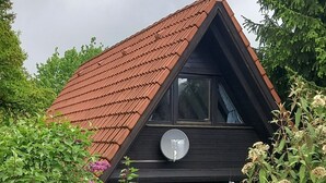 Una casa de techo rojo, un reloj y rodeada de vegetación.