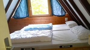 Una cama individual con ropa de cama blanca, una almohada y una manta en una habitación con paredes de madera y una ventana con cortinas azules.