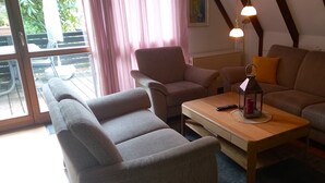 Una sala de estar acogedora con un sofá, sillones, una mesita de madera y una lámpara de pie.