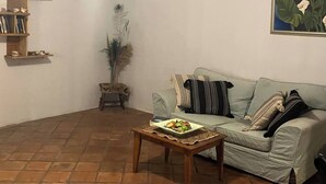 A living room with a sofa, a coffee table with fruit, a bookshelf, and a painting on the wall. - Jasmin cottage Brixton (Johannesburg)