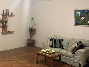 A living room with a sofa, a coffee table with fruit, a bookshelf, and a painting on the wall. - Jasmin cottage Brixton (Johannesburg)