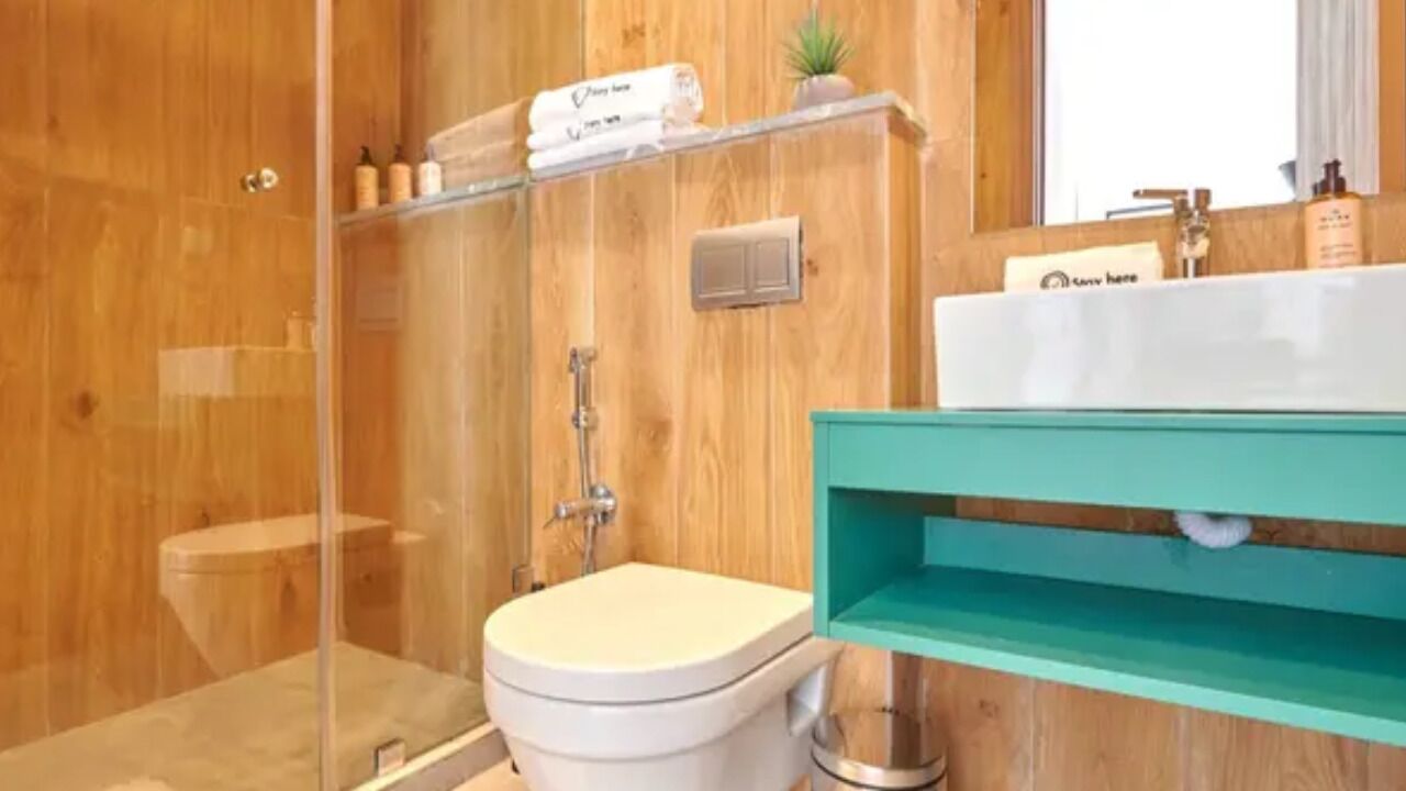 A wooden bathroom with a toilet, shower, and a sink with a mirror.