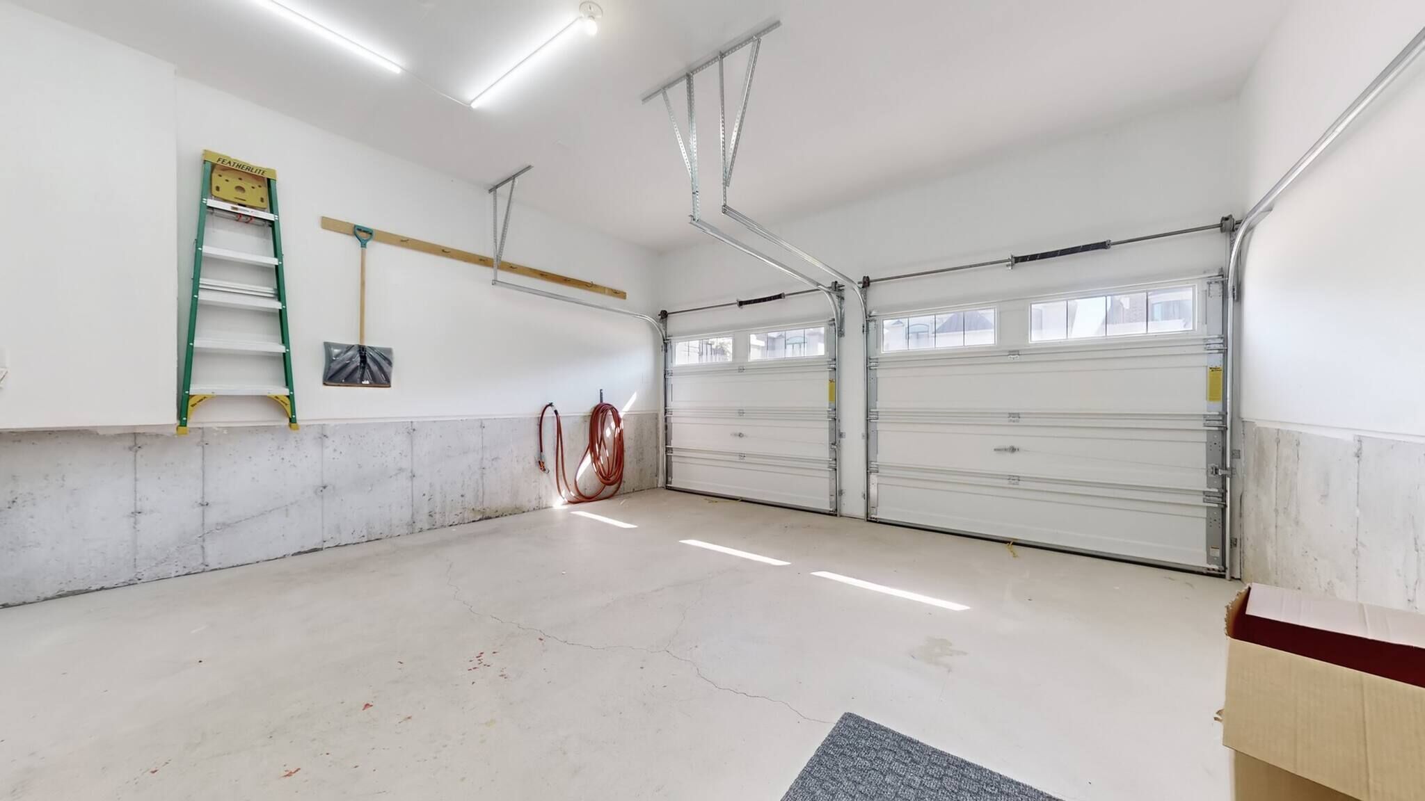 A garage with two double doors, a concrete floor, and a ladder against the wall.