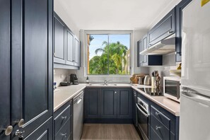 A modern kitchen with dark cabinets, a window with a view of greenery, a sink, and a stove. - Cosy Darling Point apartment (Darling Point)