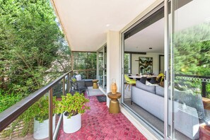 A balcony with a glass door leading to a dining area, surrounded by greenery. - Cosy Darling Point apartment (Darling Point)