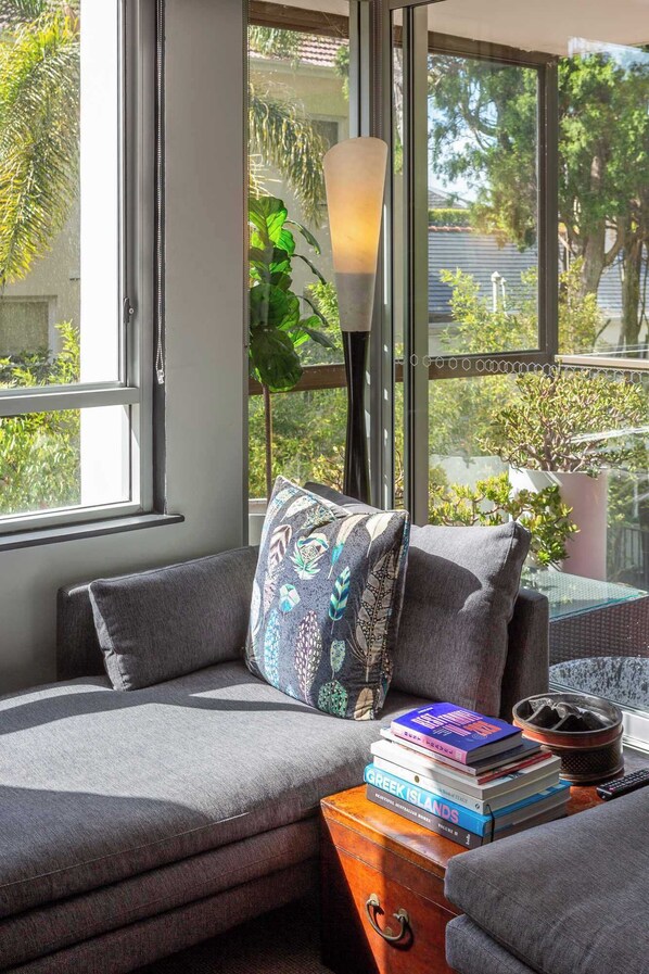A cozy seating area with a cushioned bench, a patterned pillow, and a stack of books on a wooden side table. - Cosy Darling Point apartment (Darling Point)
