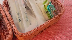 Een rieten mand met verpakte spullen op een rode tafelkleed met een patroon.