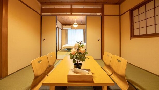 Een traditionele Japanse kamer met tatami vloeren, een lage tafel met een bloevas en schuifdeuren die naar een andere kamer leiden.