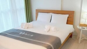 Een net opgemaakt bed met een grijs-witte spreidekking, een houten hoofdbord en een nachtkastje met een lamp.