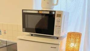 Een compacte keuken met een magnetron bovenop een koelkast, een klein spoelgedeelte en een tafel met een stoel.