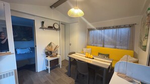 A compact living space with a dining area, a small kitchenette, a bed, and a window with curtains. - Magnificent mobile home (Messanges)