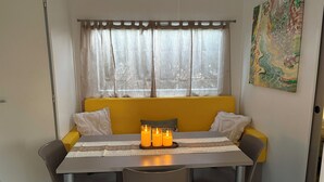 A dining area with a table, chairs, a yellow sofa, and a window with sheer curtains. - Magnificent mobile home (Messanges)
