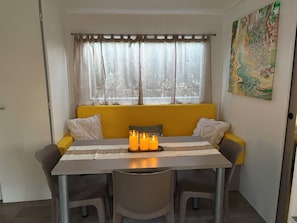A dining area with a table, chairs, a yellow sofa, and a window with sheer curtains. - Magnificent mobile home (Messanges)