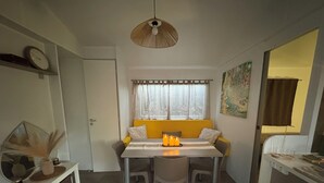 A compact room with a dining table, chairs, a hanging light fixture, a window with curtains, and a door. - Magnificent mobile home (Messanges)